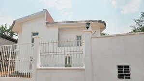 Un edificio blanco con entrada protegida por un portón, un ventanal pequeño y un balcón con barandilla de metal.