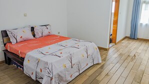 Un dormitorio con cama, piso de madera, una puerta y un ventanal con cortinas.