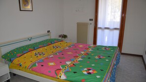 A bedroom with a bed, a nightstand, a radiator, and a window with curtains.