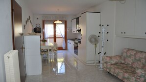 A compact kitchen with a dining area, a radiator, a sofa, and a fan.