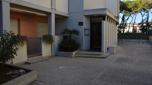 A modern building with a gated entrance, a small garden area with plants, and a paved courtyard.