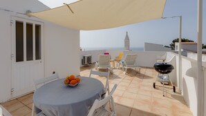 A terrace with a table, chairs, a grill, and a view of a tower. - Solemar @ Vale de Centeanes (Carvoeiro)