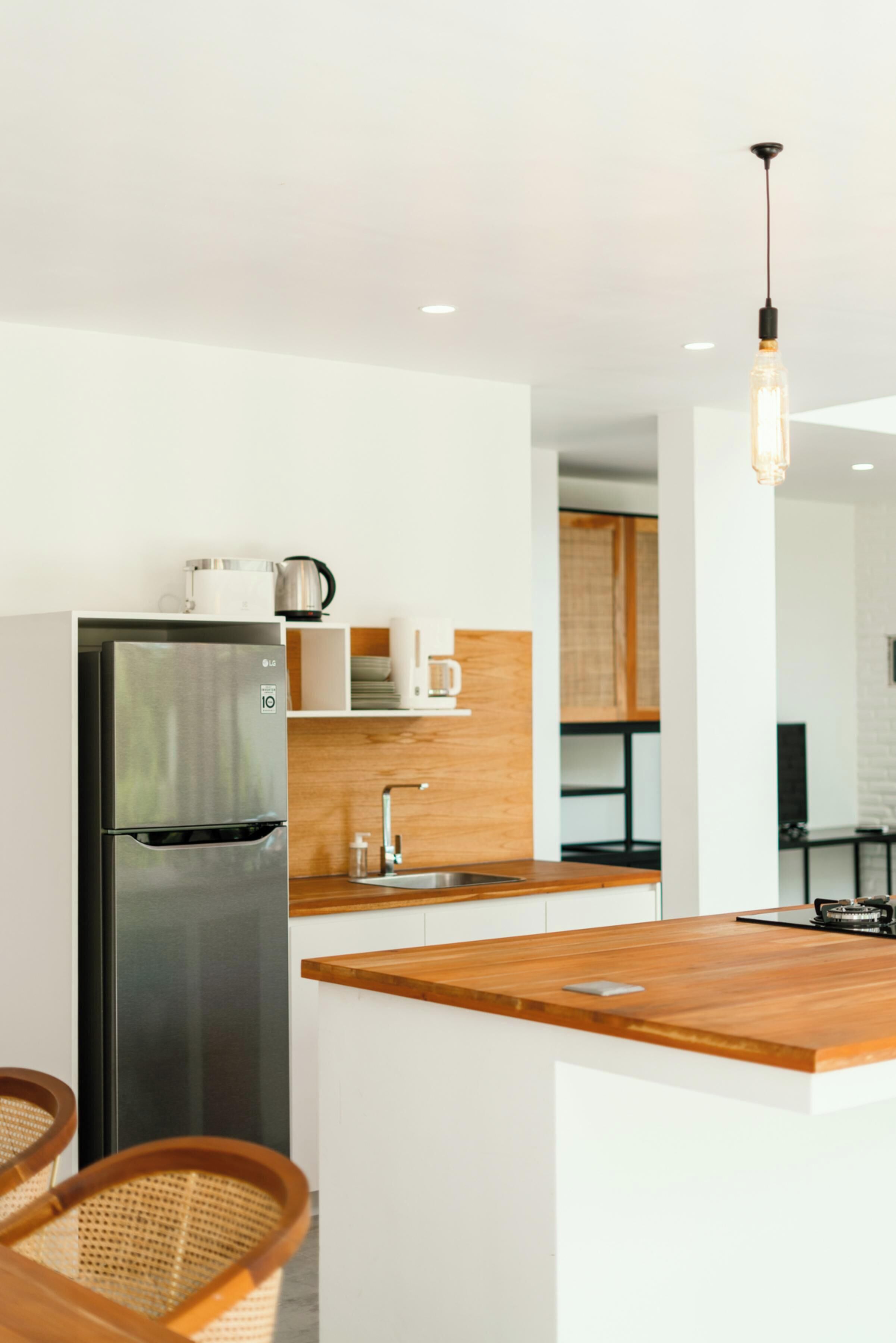 A modern kitchen with a stainless steel refrigerator, wooden countertop, and a hanging light fixture.