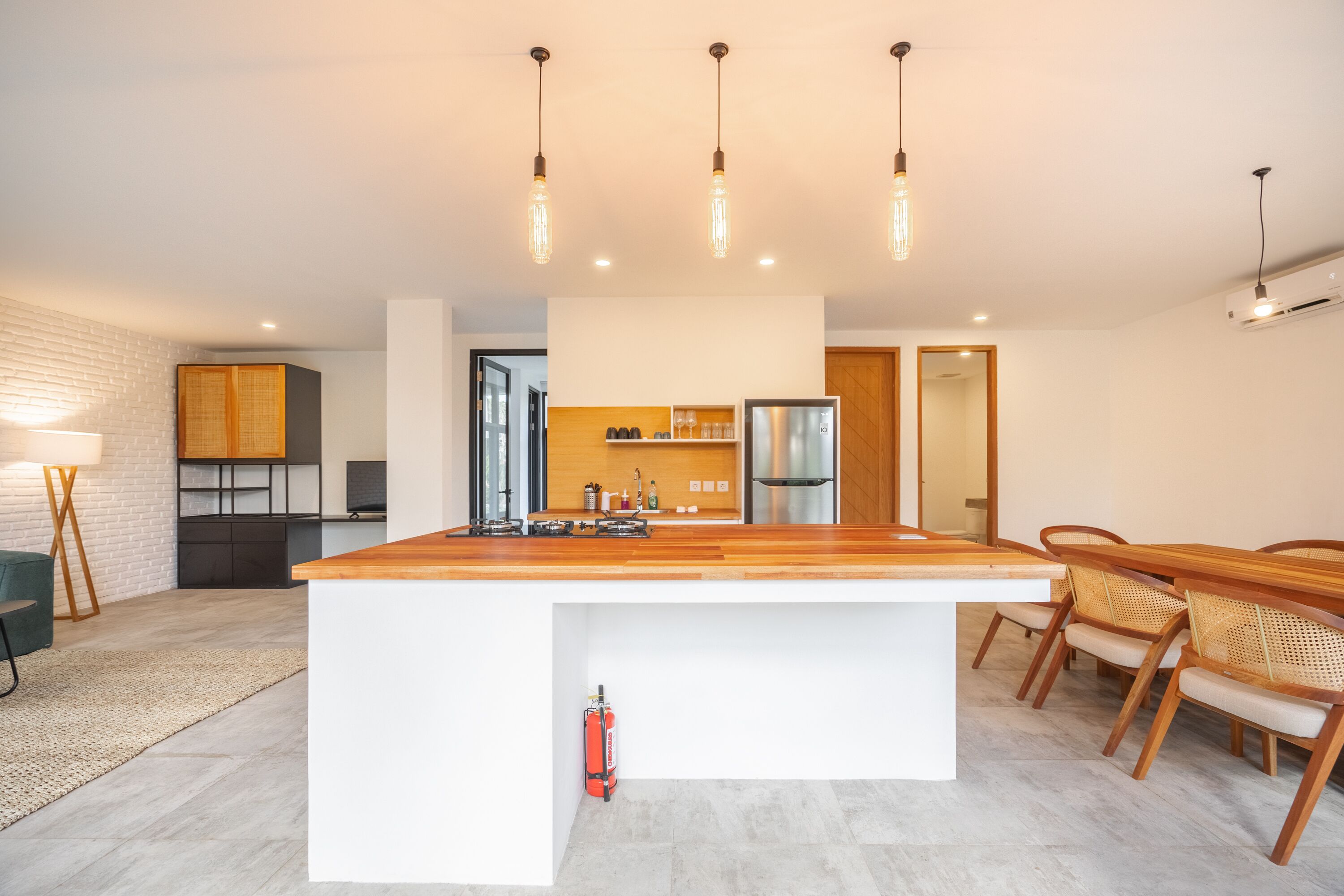 A modern kitchen with a central island, wooden chairs, and pendant lighting.