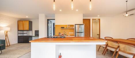 A modern kitchen with a central island, wooden chairs, and pendant lighting.