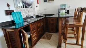 A kitchen with wooden cabinets, a black countertop, a sink, and a dining area with wooden chairs. - Lux Suites Diani Airstrip Villas  (Diani Beach)
