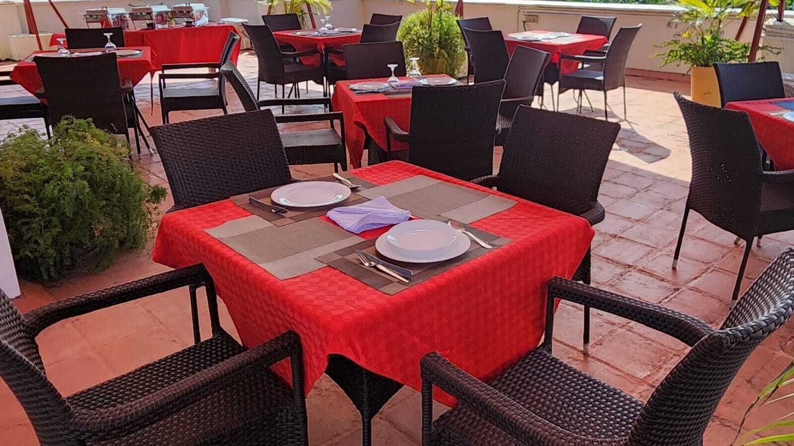 Un espace de restauration en plein air avec des tables pour deux, agrémenté de nappes rouges et de chaises en osier noir.