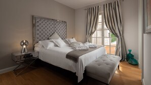 A bedroom with a large bed, a bedside table, a bench, and a window with curtains.