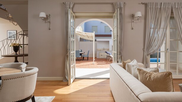 A spacious living area with a sofa, chairs, a dining table, and a view of an outdoor patio with a pool.