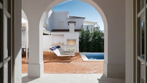 An outdoor patio with a pool, lounge chairs, and a BBQ area.