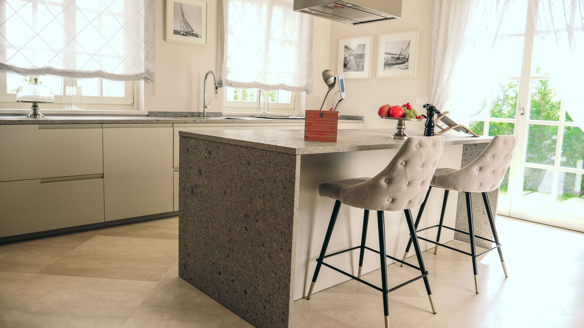 A modern kitchen with a central island, two bar stools, and a window with a view of greenery.