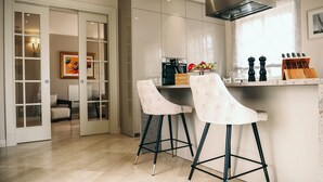 A modern kitchen with two bar stools, a countertop with kitchen appliances, and a dining area with a sofa and chairs. - Villa Fiordaliso by Villas Guide (Tar)