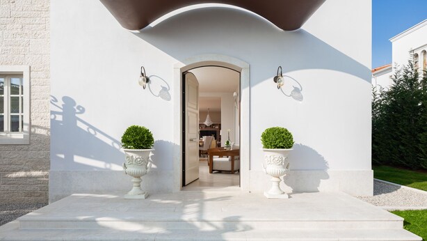 A modern house with a white exterior, a curved roof, and a doorway leading to an interior. There are two potted plants on either side of the entrance. - Villa Fiordaliso by Villas Guide (Tar)