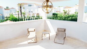 A balcony with two wicker chairs and a small table, overlooking a lush garden and white buildings with red roofs. - Villa Fiordaliso by Villas Guide (Tar)