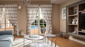 Un salon avec vue sur la piscine, un lustre, un grand miroir et un canapé bleu.