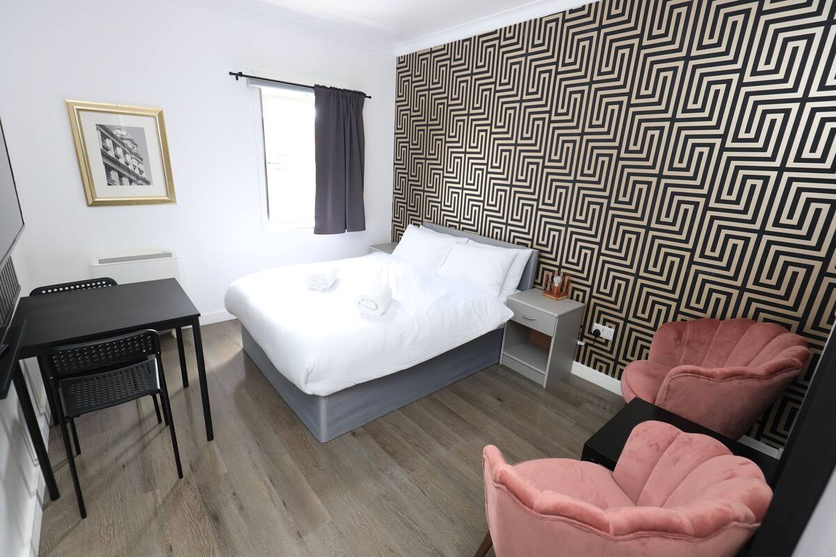 A hotel room with a bed, a desk, a chair, and a small table.