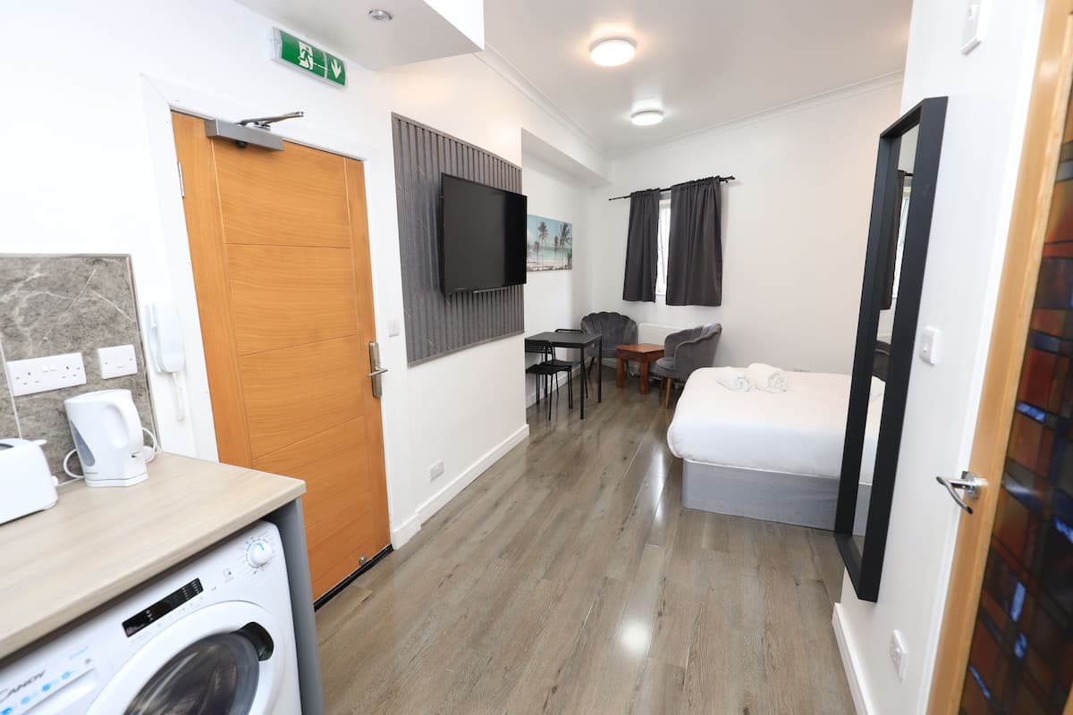A compact hotel room with a washing machine, a bed, a TV, and a small dining area.