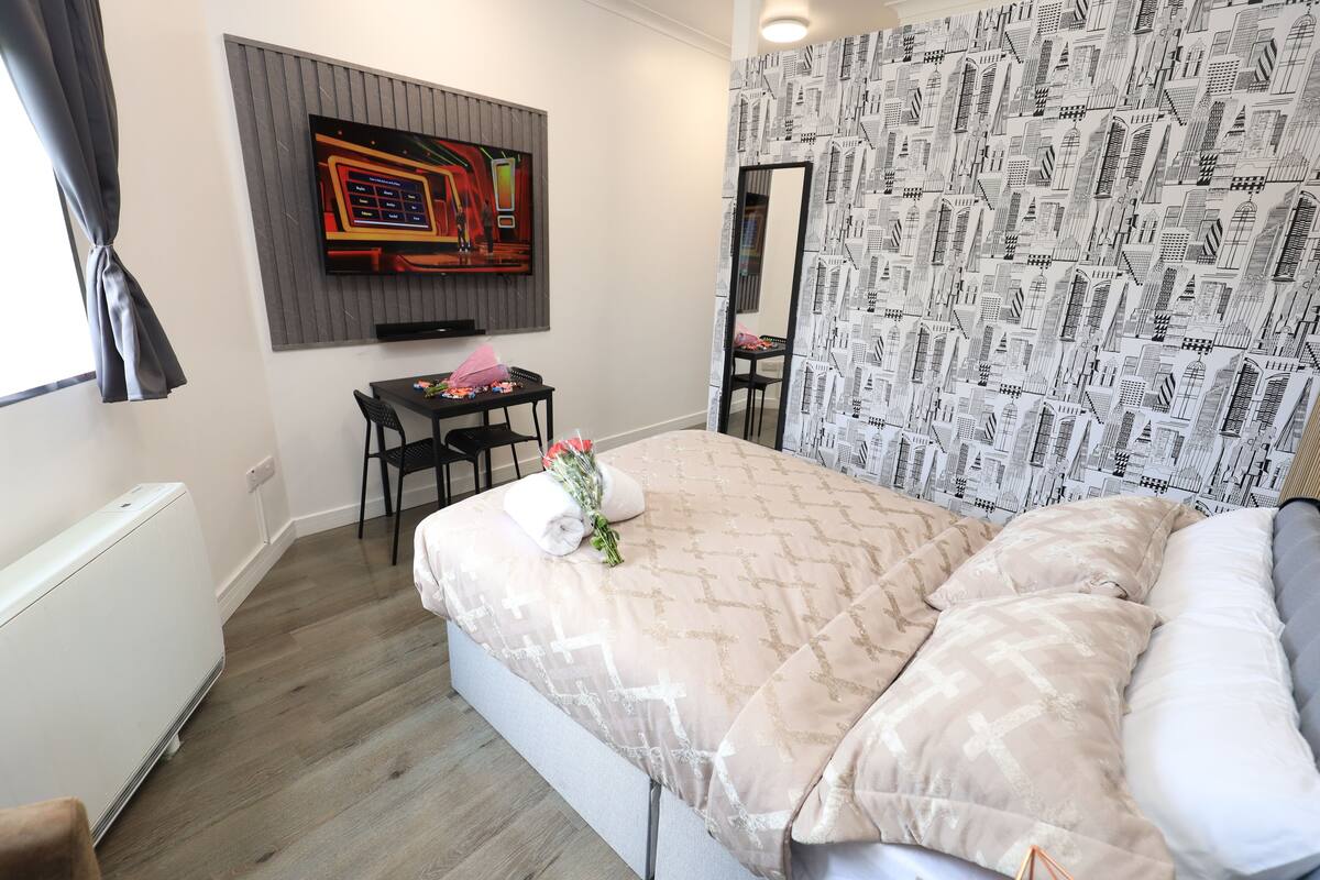 A bedroom with a bed, a desk, and a chair. There is a mirror on the wall and a window with curtains.