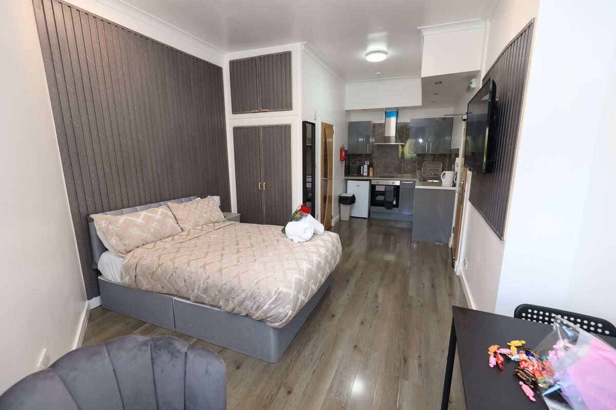 A bedroom with a bed, a small desk, and a kitchenette.