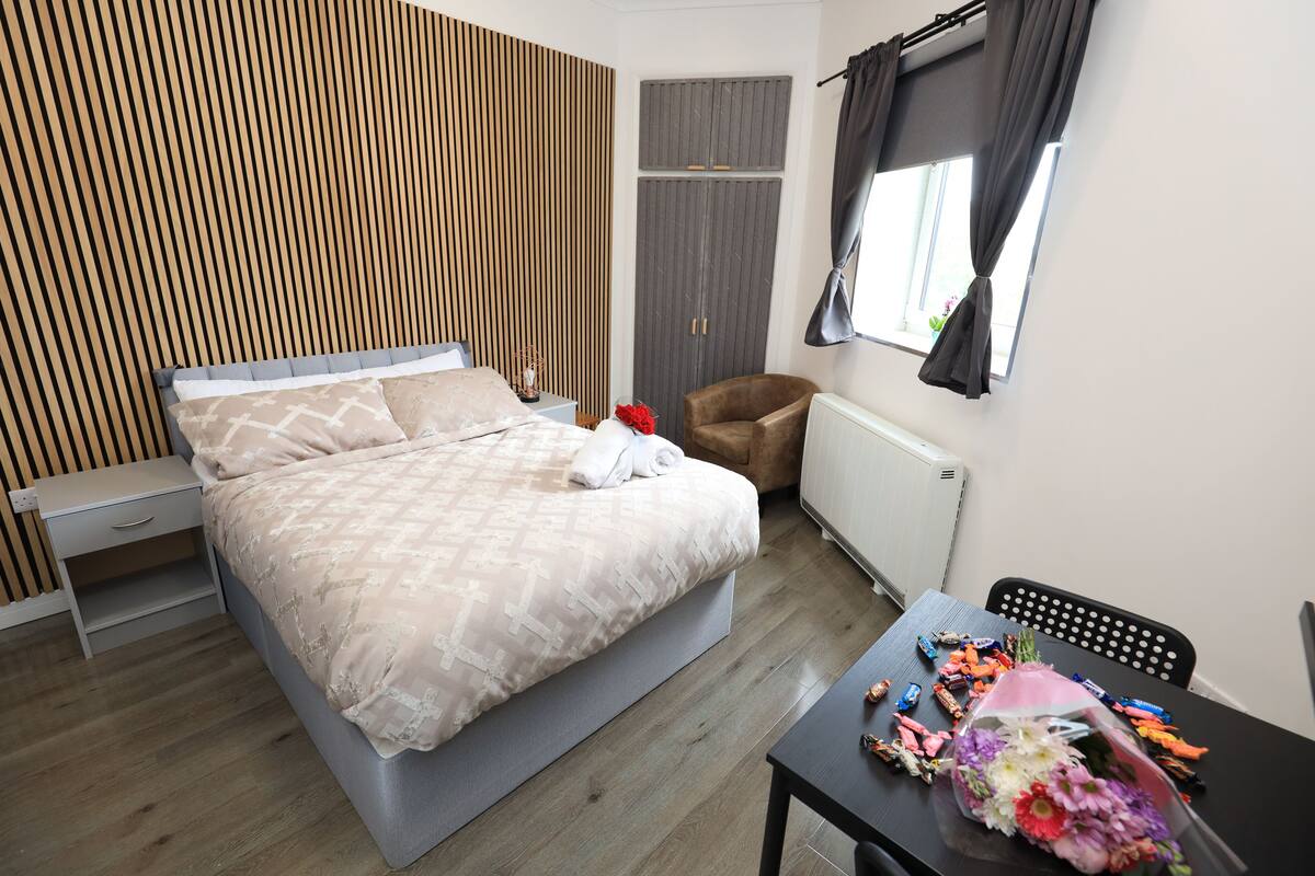 A modern bedroom with a bed, a chair, a table with snacks, and a window with curtains.