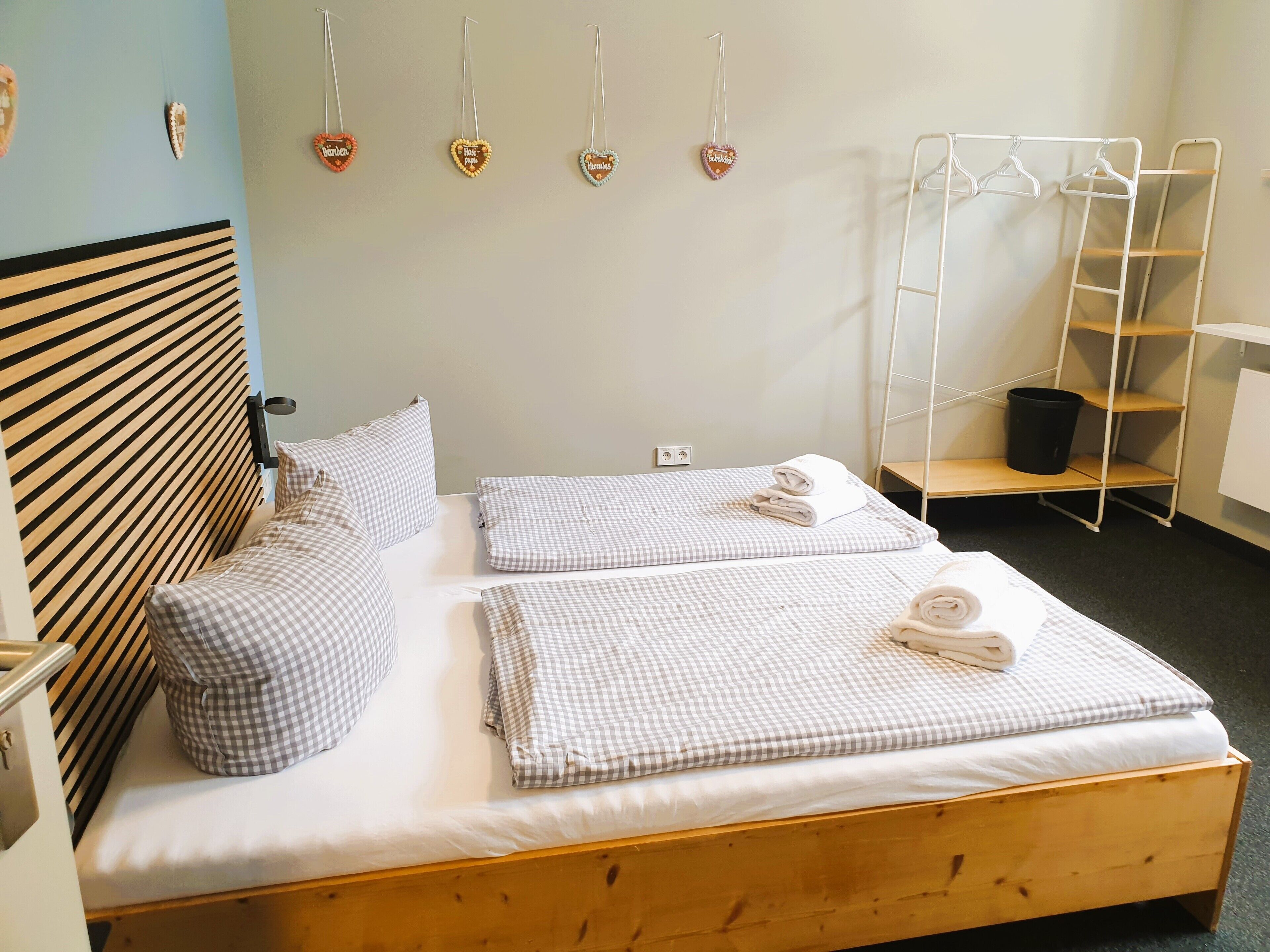 Una cama bien tendida con ropa de cama a cuadros, un cabecero de madera y un perchero de pared con adornos con forma de corazón.