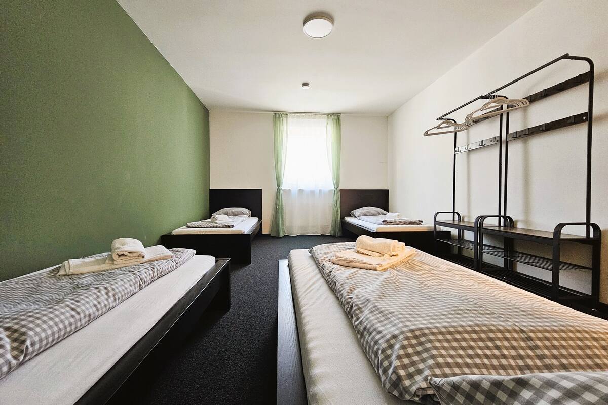 A hotel room with two single beds, a bunk bed, a desk, and a mirror.