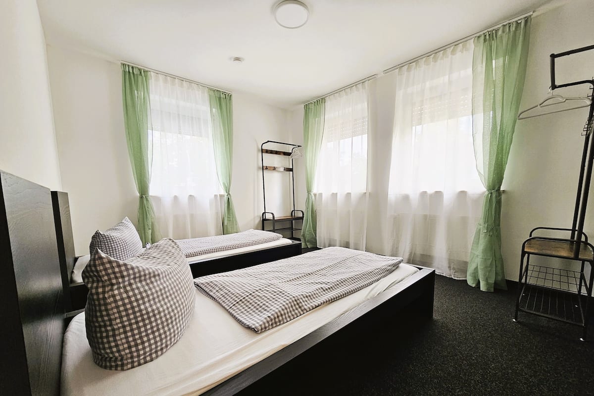 A double bed with checkered bedding, two bedside tables, a mirror, and a wardrobe with a hanging rack.