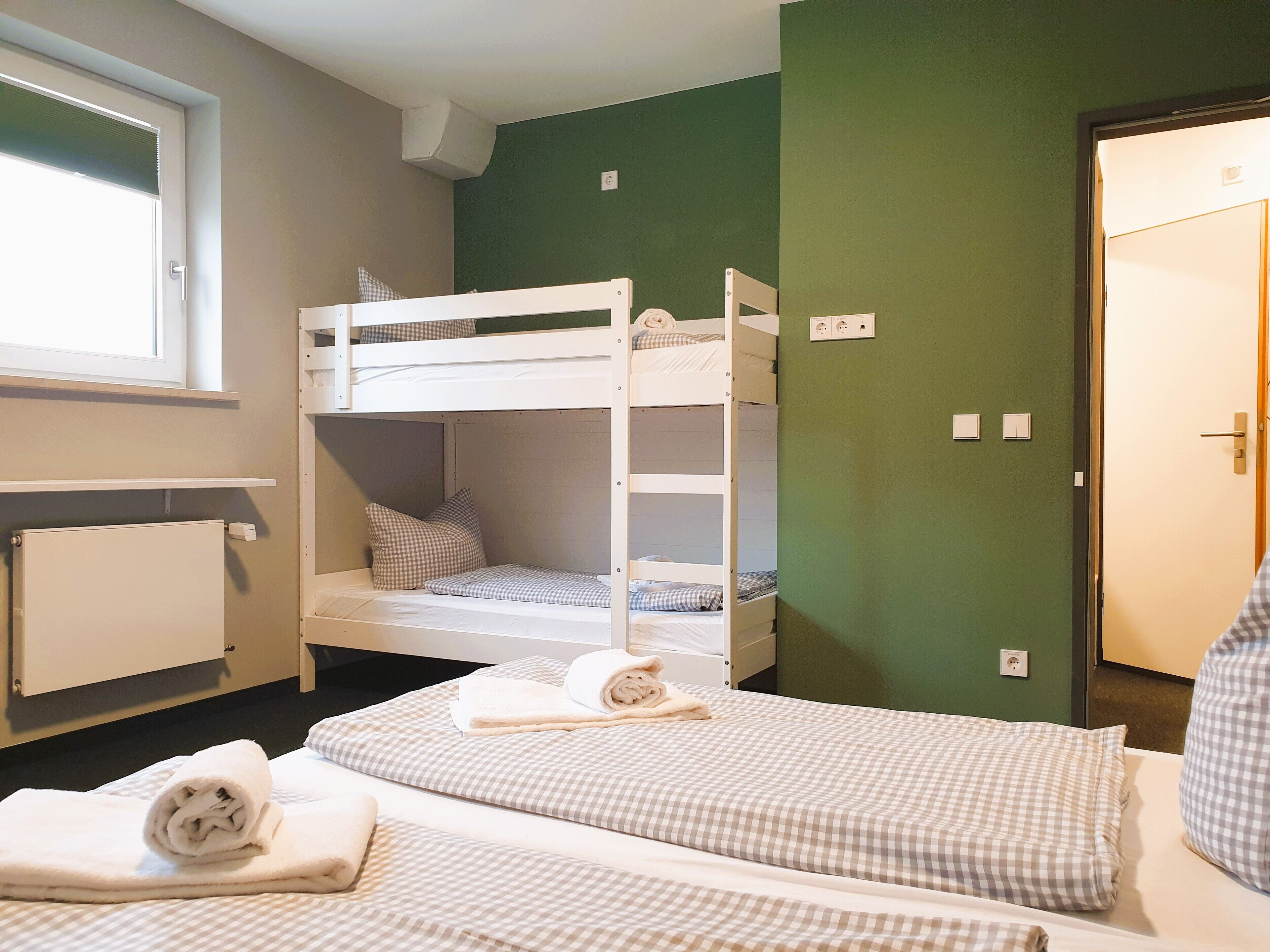 Une pièce avec des lits superposés, une fenêtre, un radiateur et une porte.