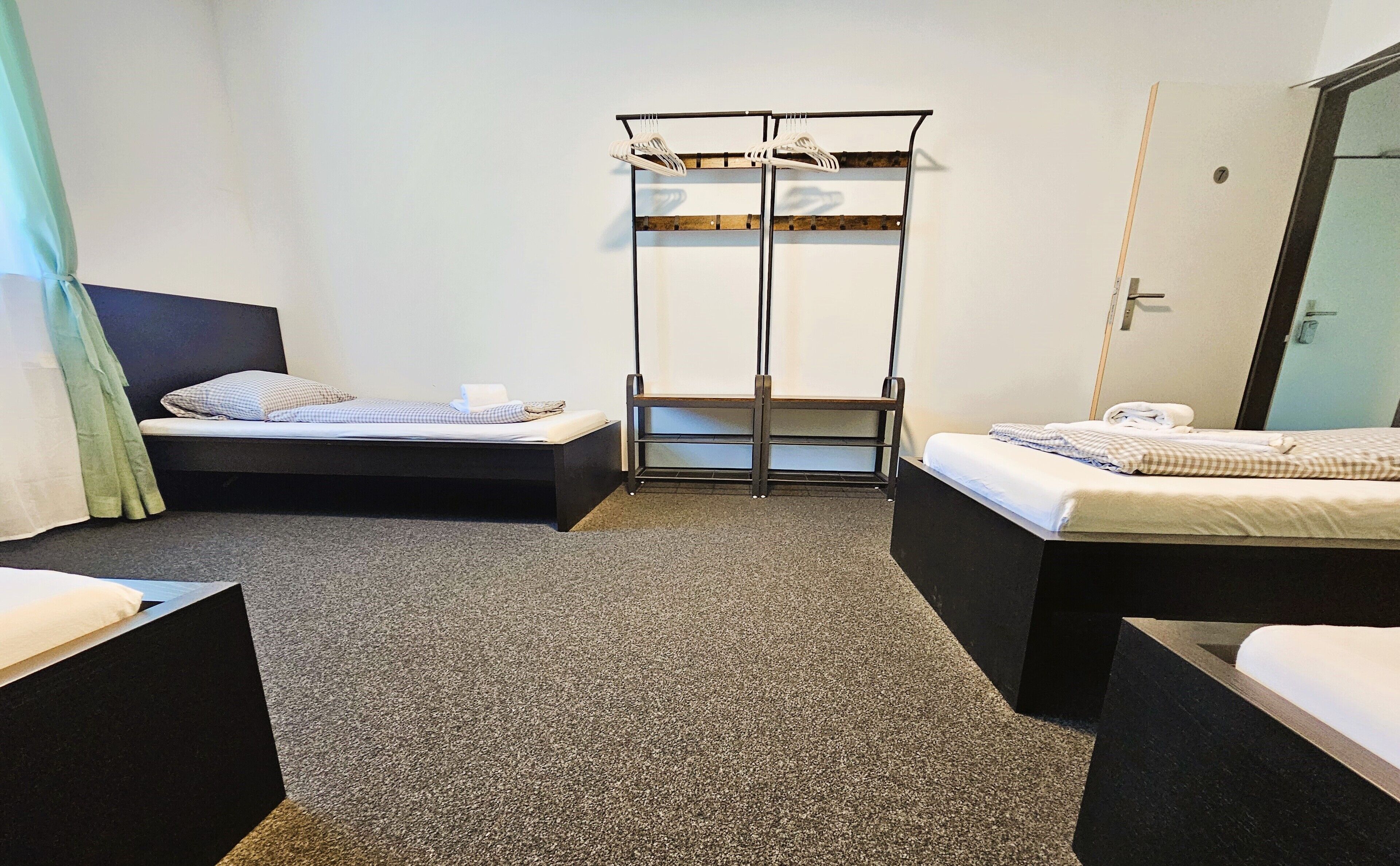 Une chambre d’hôtel avec deux lits simples, un banc en bois et un porte-manteau.