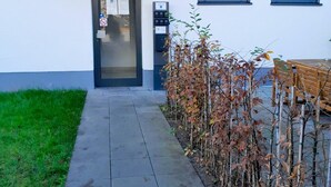 A building entrance with a door, a mailbox, and a small garden area with leafless plants. - ARRIVEL Apartments Moosfeld (Munich)