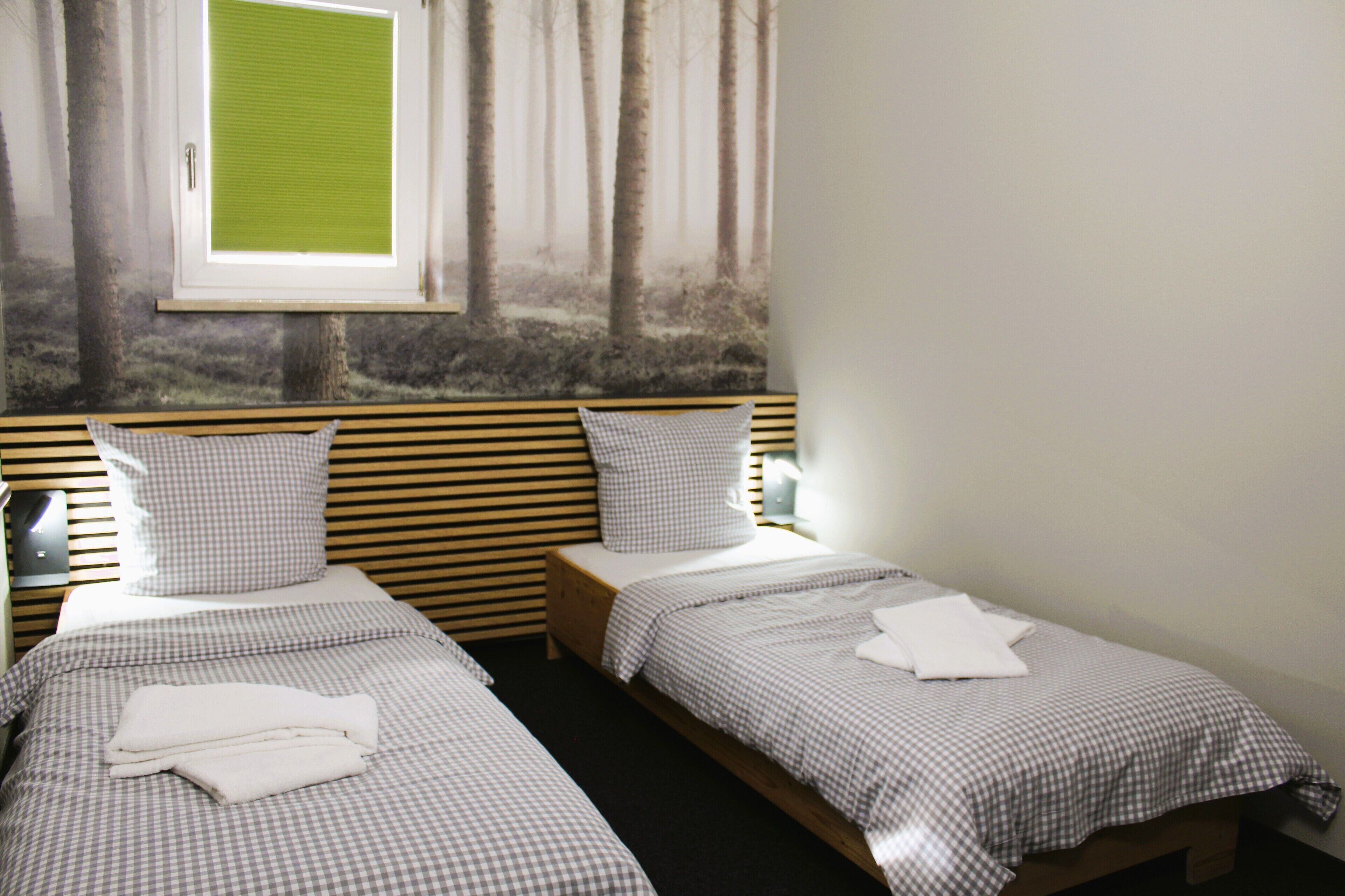 Una habitación con dos camas individuales, cada una con ropa de cama y almohadas a cuadros, un ventanal con vistas a árboles y un cabecero de madera.
