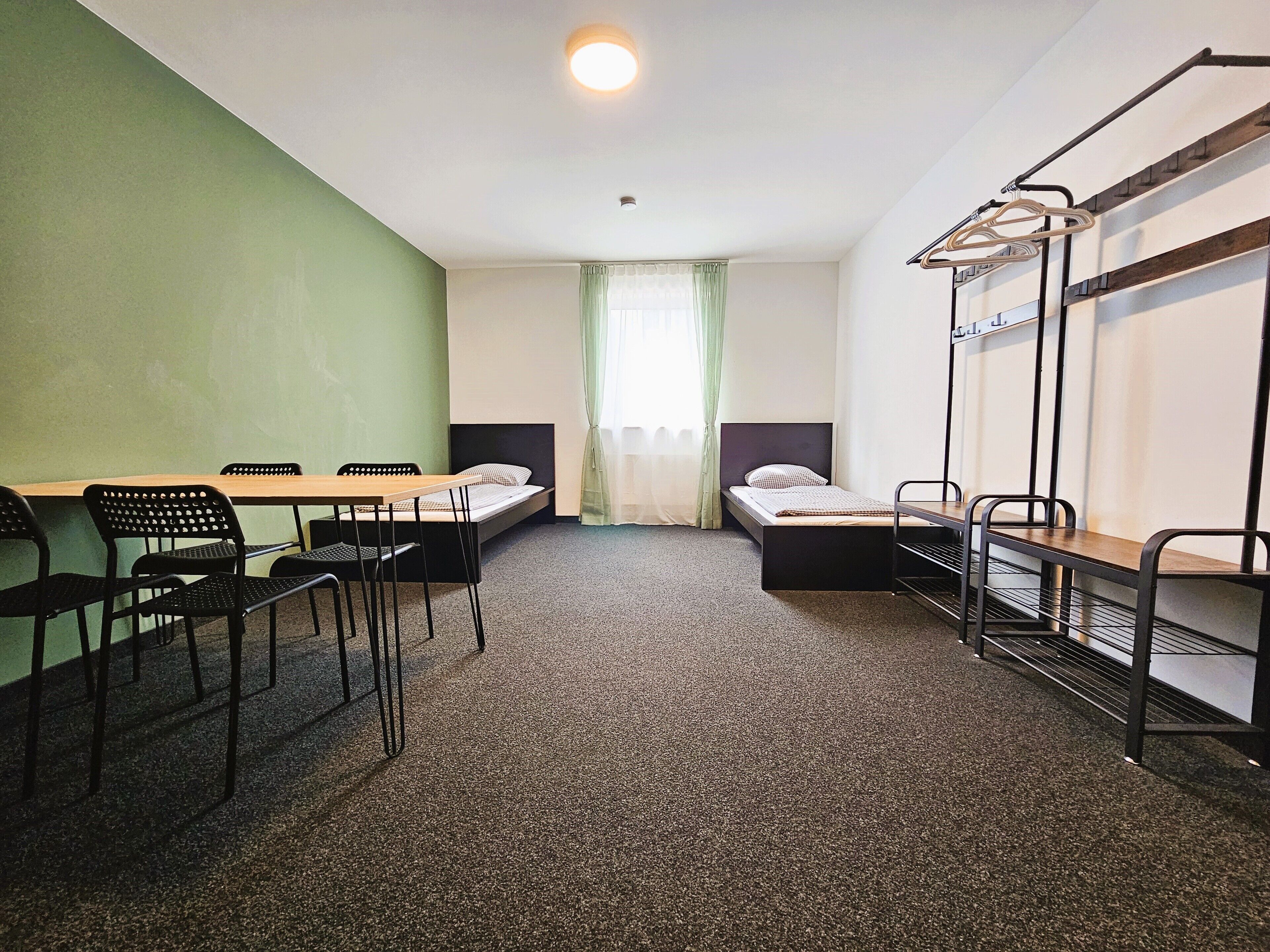 Una camera del dormitorio con letti a castello, un tavolo, sedie e un appendiabiti.