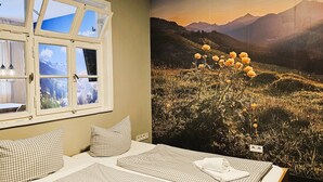 A room with a large window, checkered pillows, a neatly made bed, and a wall-mounted light fixture. - ARRIVEL Apartments Moosfeld (Munich)
