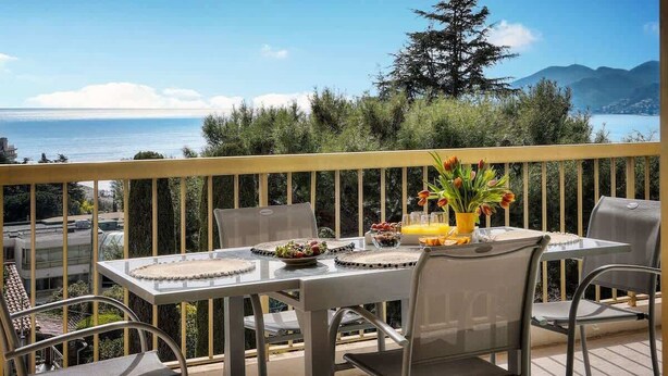 Un balcón con una mesa para dos, con vistas panorámicas al mar y a las montañas.