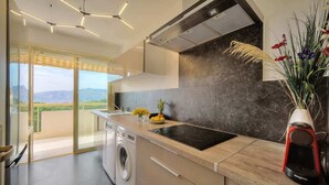 Una cocina moderna con lavadora incorporada, un ventanal con vistas al campo y una planta decorativa sobre la encimera.