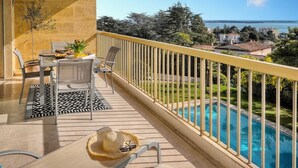 Un balcón con piscina, mobiliario exterior y vistas al mar y edificios circundantes.