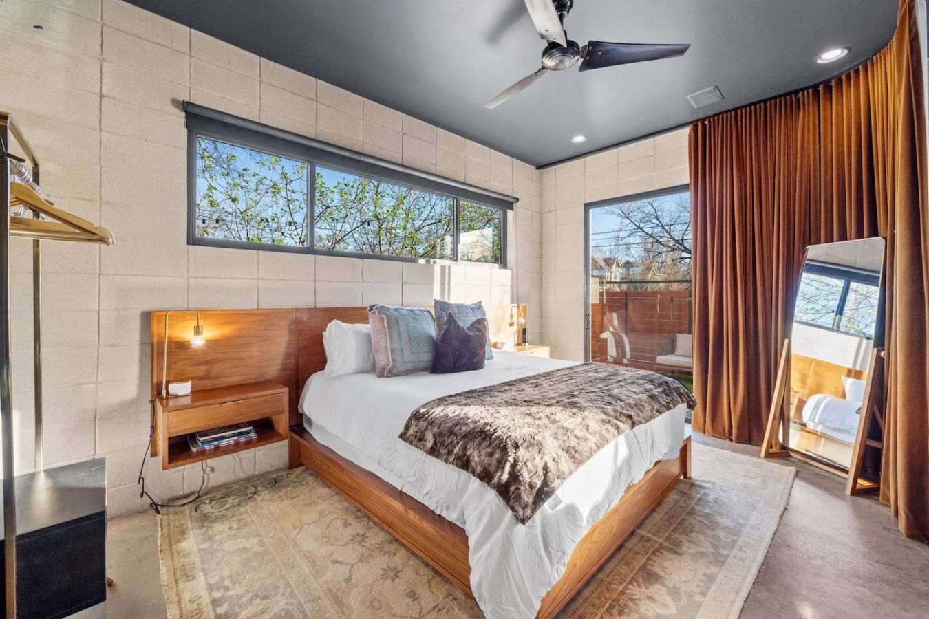 A modern bedroom with a large bed, a ceiling fan, and a view of the outdoors through a window.