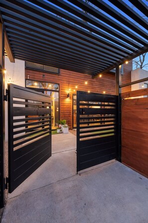 Une entrée moderne avec une façade en bois, un porche abrité et une allée menant à une porte grillagée.