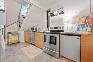 Una cucina moderna con forno a incasso, frigorifero e microonde. Una scala conduce a un piano superiore.