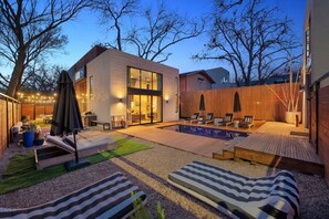 Un'area esterna moderna con piscina, poltrona relax e terrazza in legno.