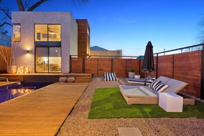 Een modern huis met een zwembad, buitenzitplaatsen en een houten terras.