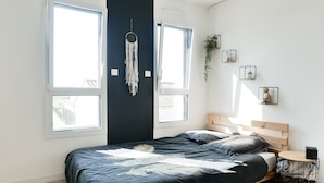A modern bedroom with a large bed, a wooden headboard, and a small bedside table. There are two windows providing natural light, and a wall-mounted dreamcatcher. - New house, swimming pool, near the ocean Les Sables 7 pers (Les Sables-d´Olonne)