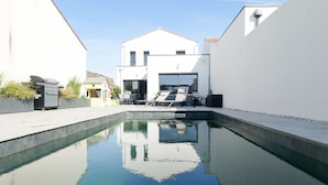 A swimming pool with a reflection of a building and a chair. - New house, swimming pool, near the ocean Les Sables 7 pers (Les Sables-d´Olonne)