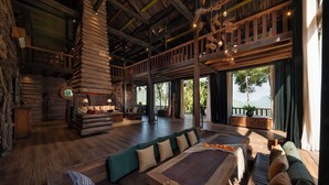 A spacious log cabin interior with a large wooden dining table, multiple seating areas, and a balcony with a view of the outdoors. - P'apiu Resort (Ngoc Duong)