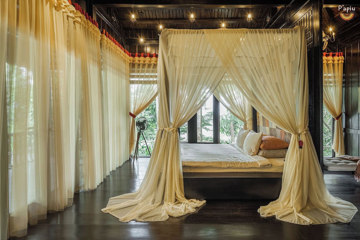 A bedroom with a canopy bed, large windows, and a view of greenery outside.