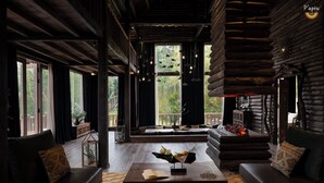 A log cabin interior with a cozy seating area, a fireplace, and large windows offering a view of the outdoors. - P'apiu Resort (Ngoc Duong)