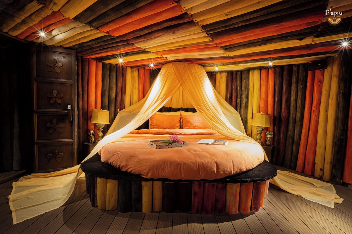 A circular bed with a canopy, wooden walls, and a wooden floor.