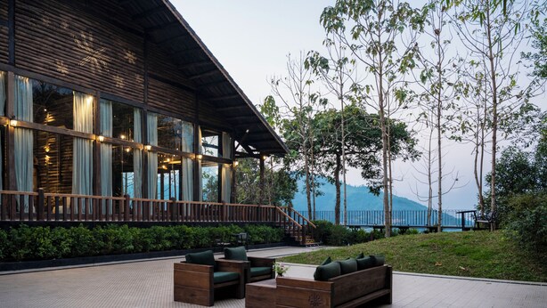 A wooden building with large windows, outdoor seating, and a view of a body of water.
