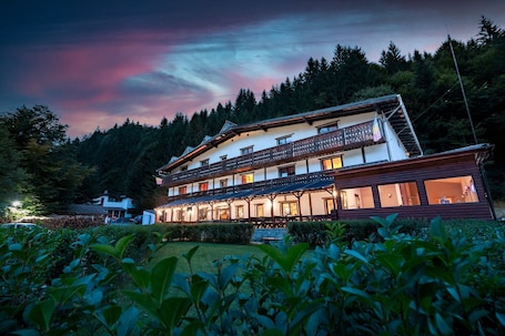 A two-story building with balconies, surrounded by greenery and trees.