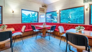 A restaurant with red cushioned seating, wooden tables, and large windows offering views of a cabin and forest. - RESORT 7 CRAI (Zarnesti)